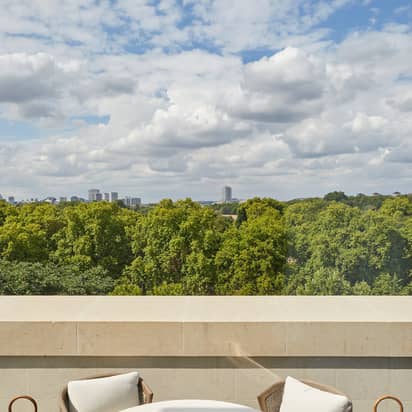 A round white table with a blue ceramic on the terrace with two arm chairs and white cushions overlooking Hyde Park