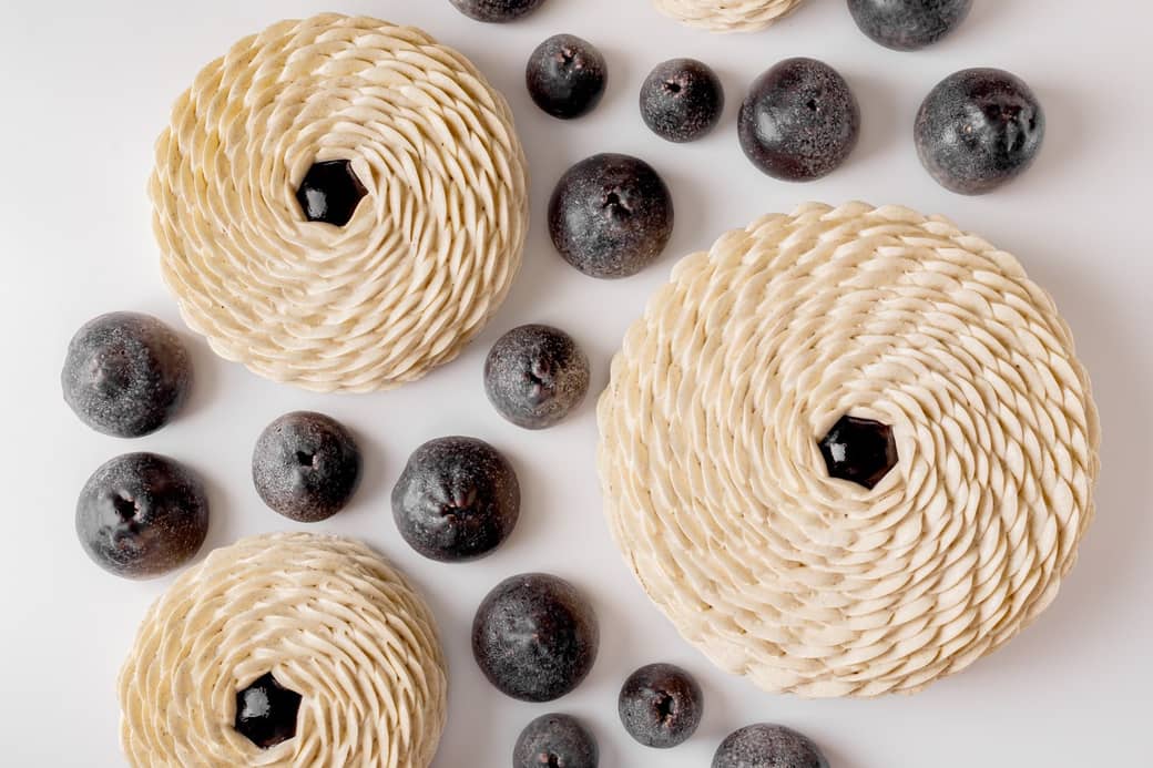 An artistic arrangement of intricately layered pastries with spiral patterns, paired with dark, round fruit-like elements on a pristine white background, creating a visually striking contrast.