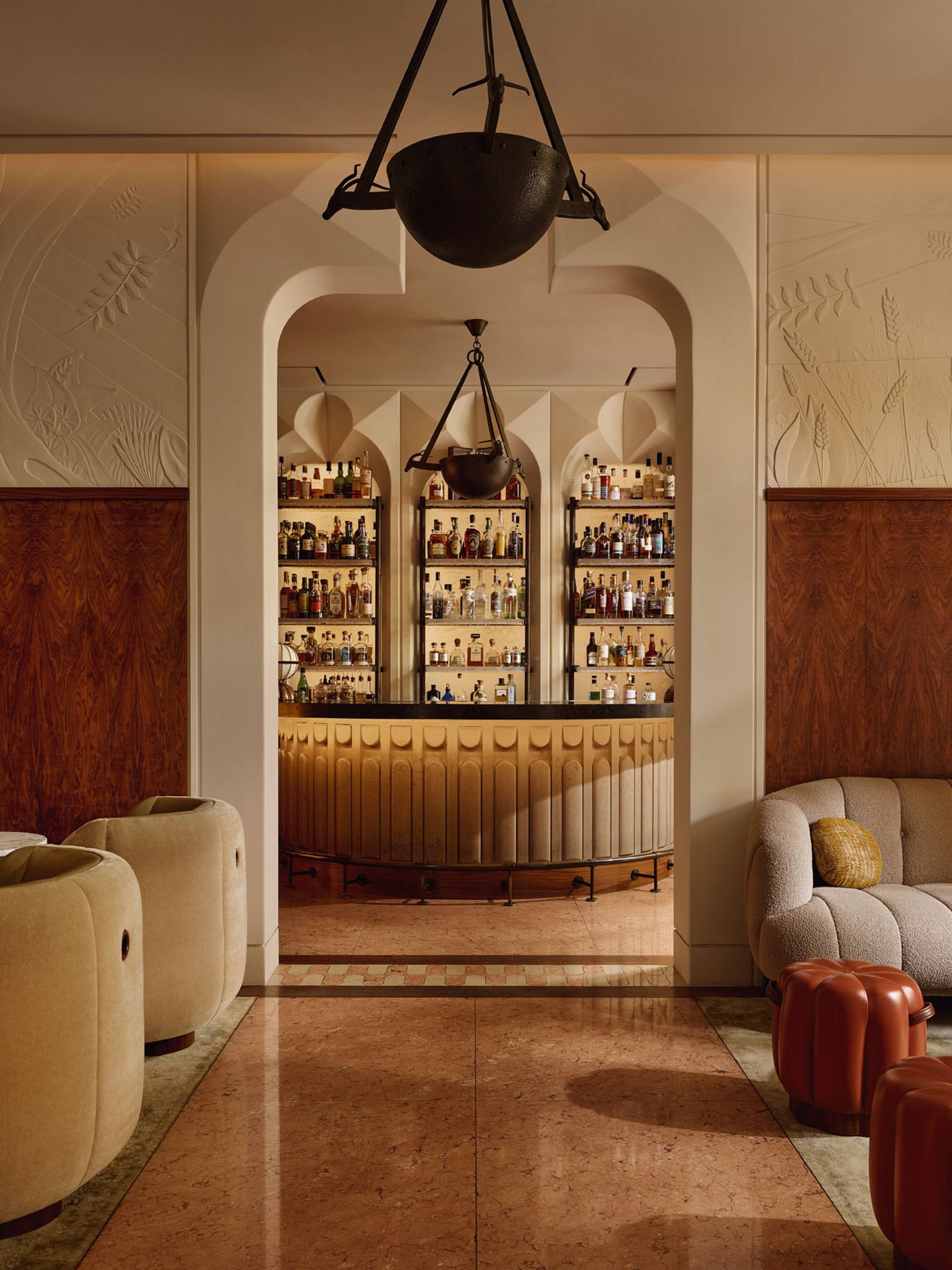 Elegant bar interior with backlit shelves of spirits, arched doorway, leather chairs, and soft ambient lighting.