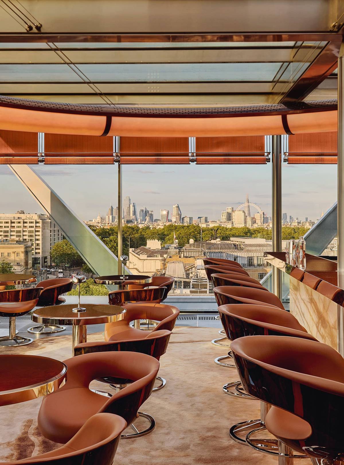 The Emory Rooftop bar, circular tables and brown leather chairs are placed in a bright room with views of the London skyline