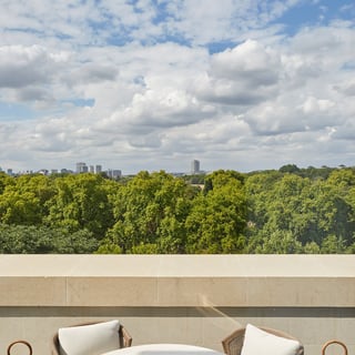 A round white table with a blue ceramic on the terrace with two arm chairs and white cushions overlooking Hyde Park